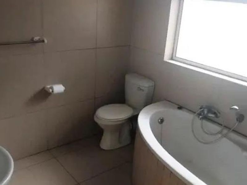 A functional bathroom featuring a bathtub, toilet, and basin with neutral wall and floor tiling, providing a clean and practical space.