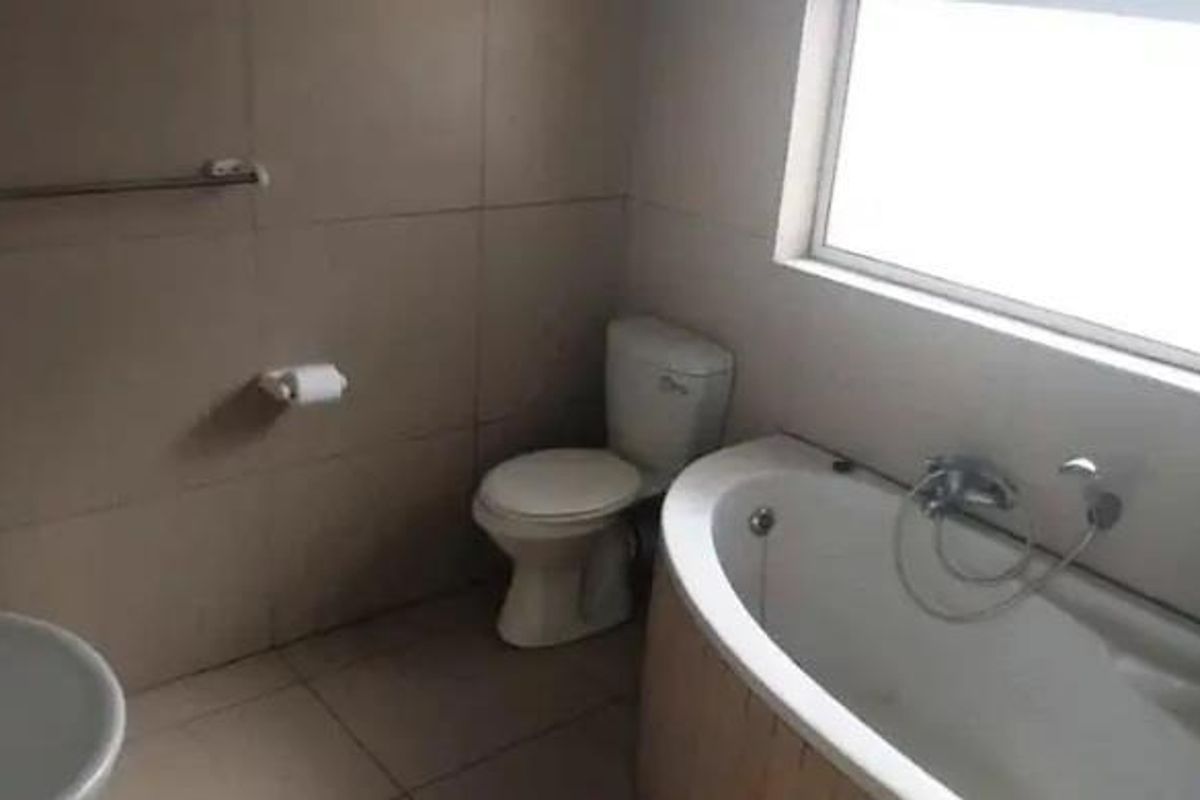 A functional bathroom featuring a bathtub, toilet, and basin with neutral wall and floor tiling, providing a clean and practical space.