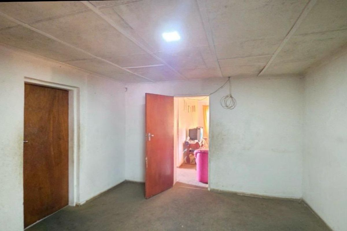 An empty bedroom featuring plain walls, a tiled ceiling, and wooden doors, requiring cosmetic updates and repairs to finishes.