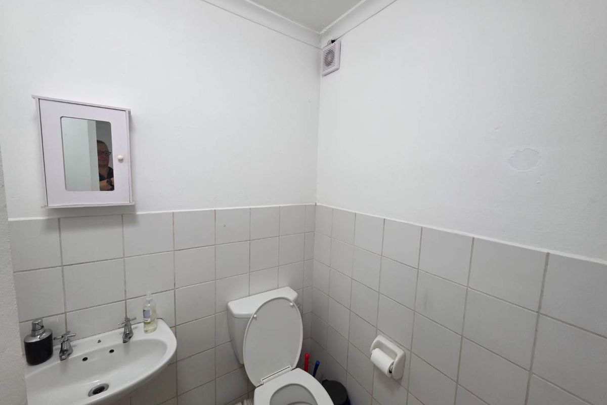 A compact bathroom featuring a wall-mounted basin, toilet, and extractor fan, finished with half-height wall tiling.
