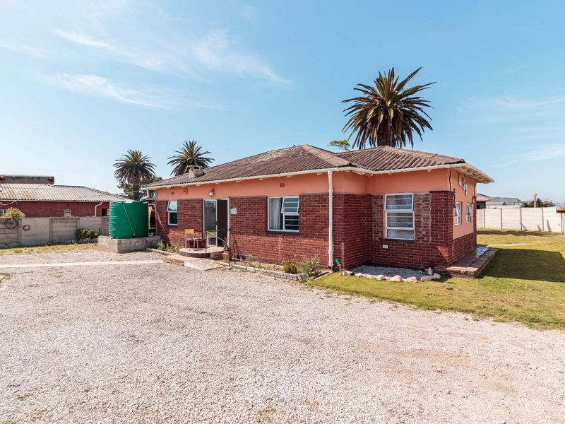 Rear view of a single-story brick house featuring a water storage tank, gravel yard, and perimeter boundary walling.