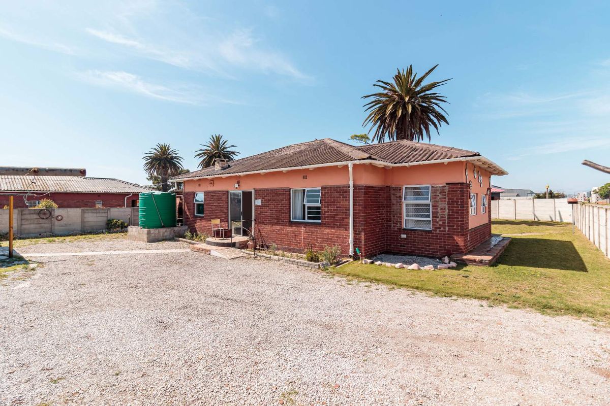 Rear view of a single-story brick house featuring a water storage tank, gravel yard, and perimeter boundary walling.
