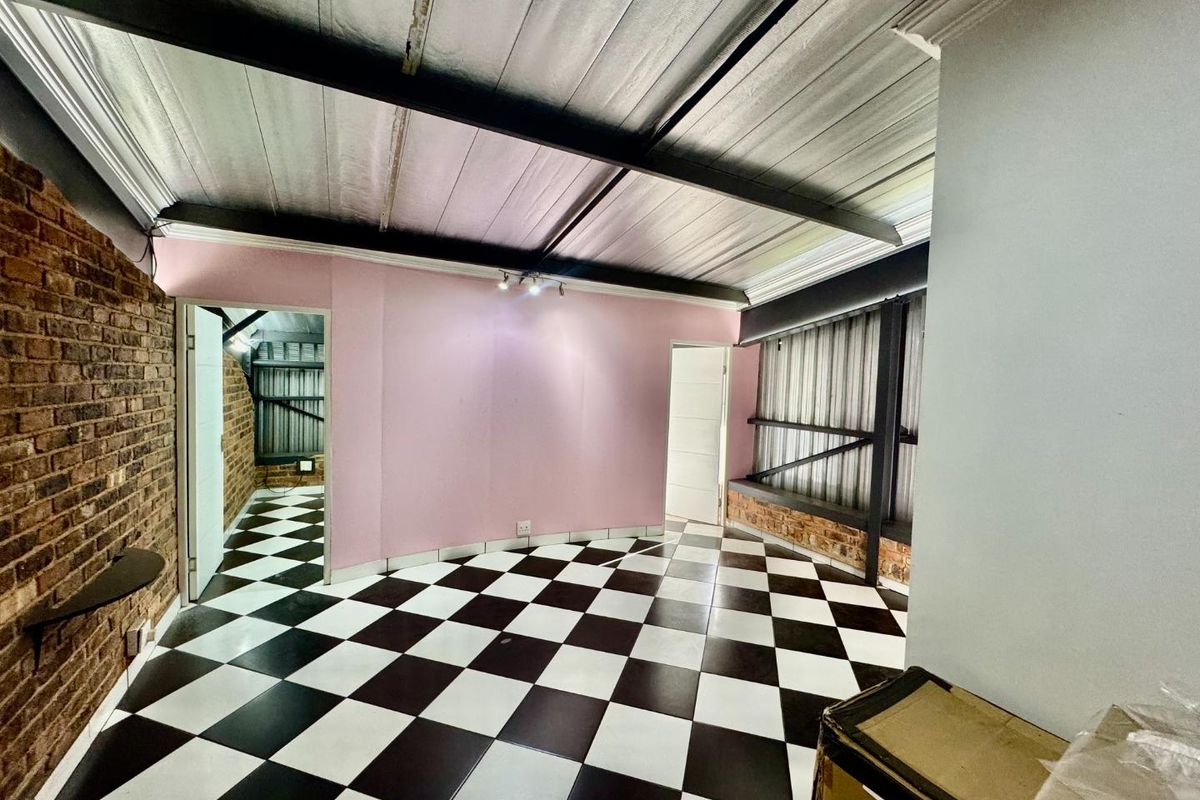 An interior view of a room featuring exposed metal ceiling beams, a brick feature wall, and black and white checkered floor tiles.