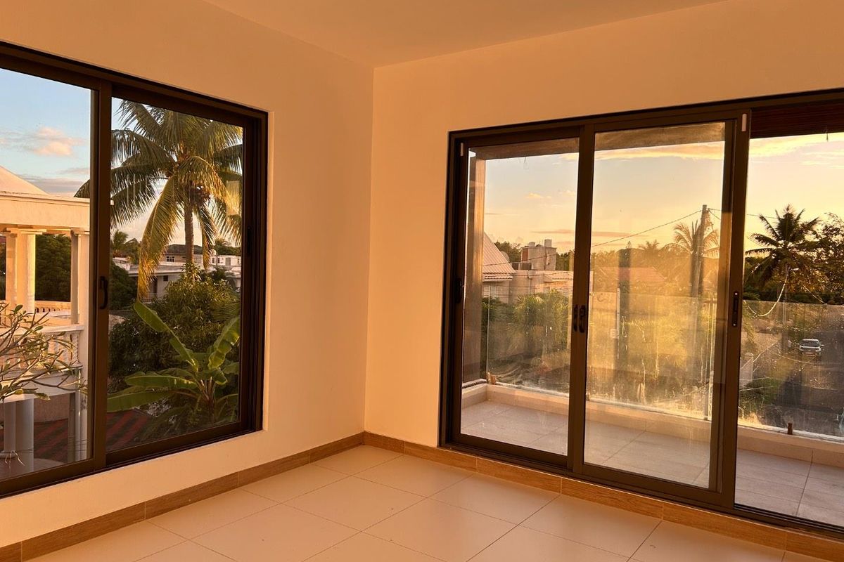 A bright, empty living area featuring large sliding glass doors that open onto a balcony, offering natural light and scenic outdoor views.