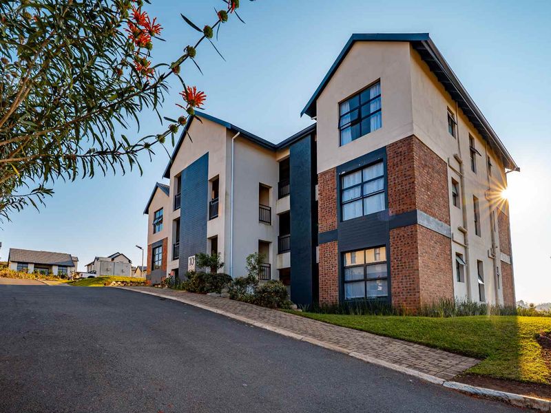 A well-maintained multi-story apartment building featuring a modern brick and plaster facade, set within a landscaped estate with paved driveway access.