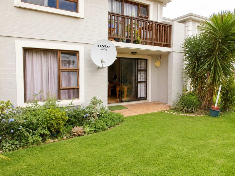 Rear view of the apartment featuring a ground-floor tiled patio, a first-floor balcony with wooden railing, and a well-maintained private garden.