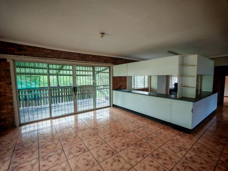 Spacious open-plan living area featuring tiled floors, exposed brick accents, and large sliding doors leading to an outdoor space with security bars.