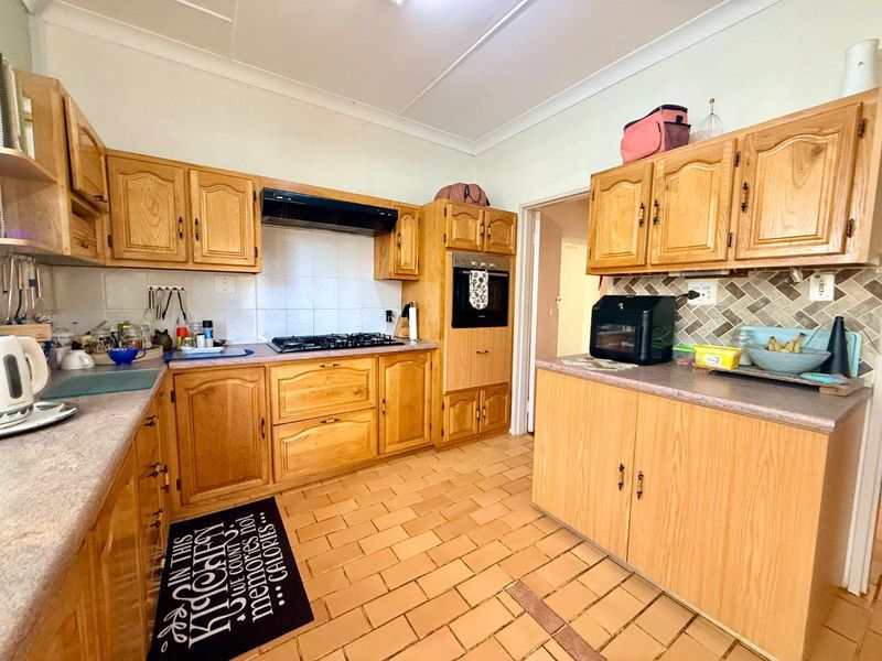 A functional kitchen featuring traditional wooden cabinetry, a gas hob, built-in oven, and tiled flooring with ample counter space.