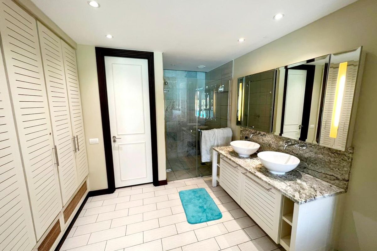 Modern bathroom featuring a double vanity with granite countertops, vessel sinks, a glass-enclosed shower, and built-in louvered cabinetry for ample storage.