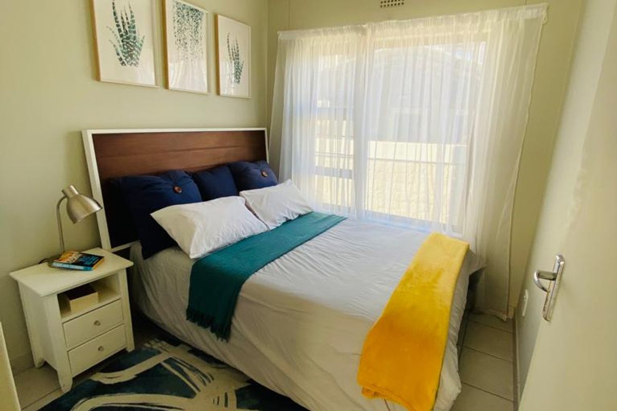 A compact bedroom featuring tiled flooring, a large window with sheer curtains, and a neutral wall finish.