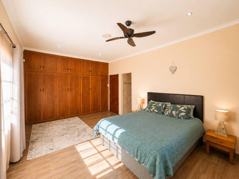 Spacious bedroom featuring extensive built-in wooden cabinetry, tiled flooring, and a ceiling fan, offering ample storage and a comfortable living environment.