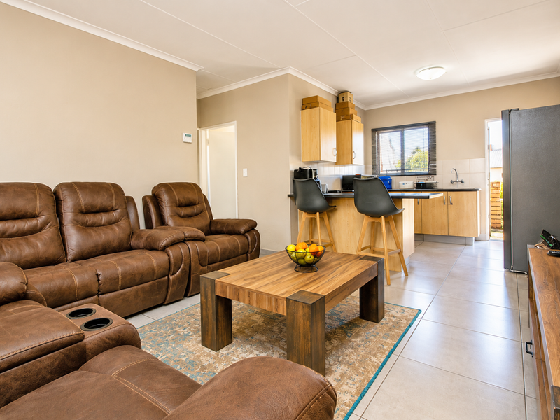 Open-plan living and kitchen area featuring tiled flooring, neutral walls, and functional kitchen cabinetry with a breakfast bar.