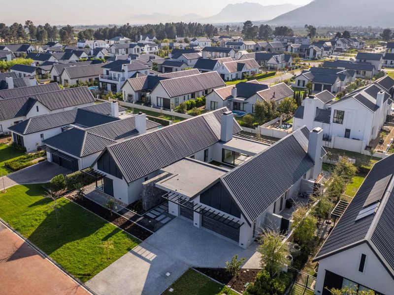 Aerial view of a modern residential property featuring a metal roof, double garage, and landscaped garden within a well-maintained estate.