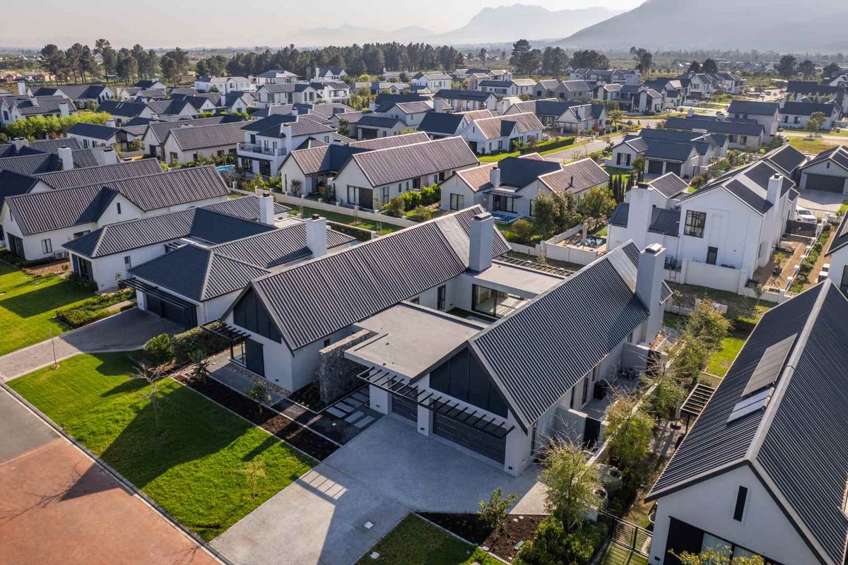 Aerial view of a modern residential property featuring a metal roof, double garage, and landscaped garden within a well-maintained estate.