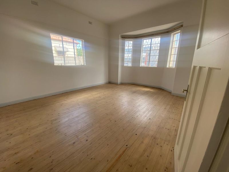 A bright, empty living room featuring polished timber flooring and a large bay window that provides ample natural light.