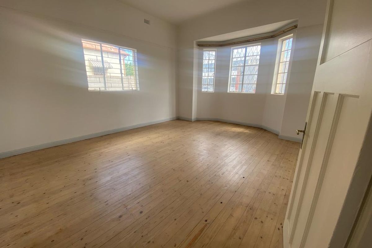 A bright, empty living room featuring polished timber flooring and a large bay window that provides ample natural light.