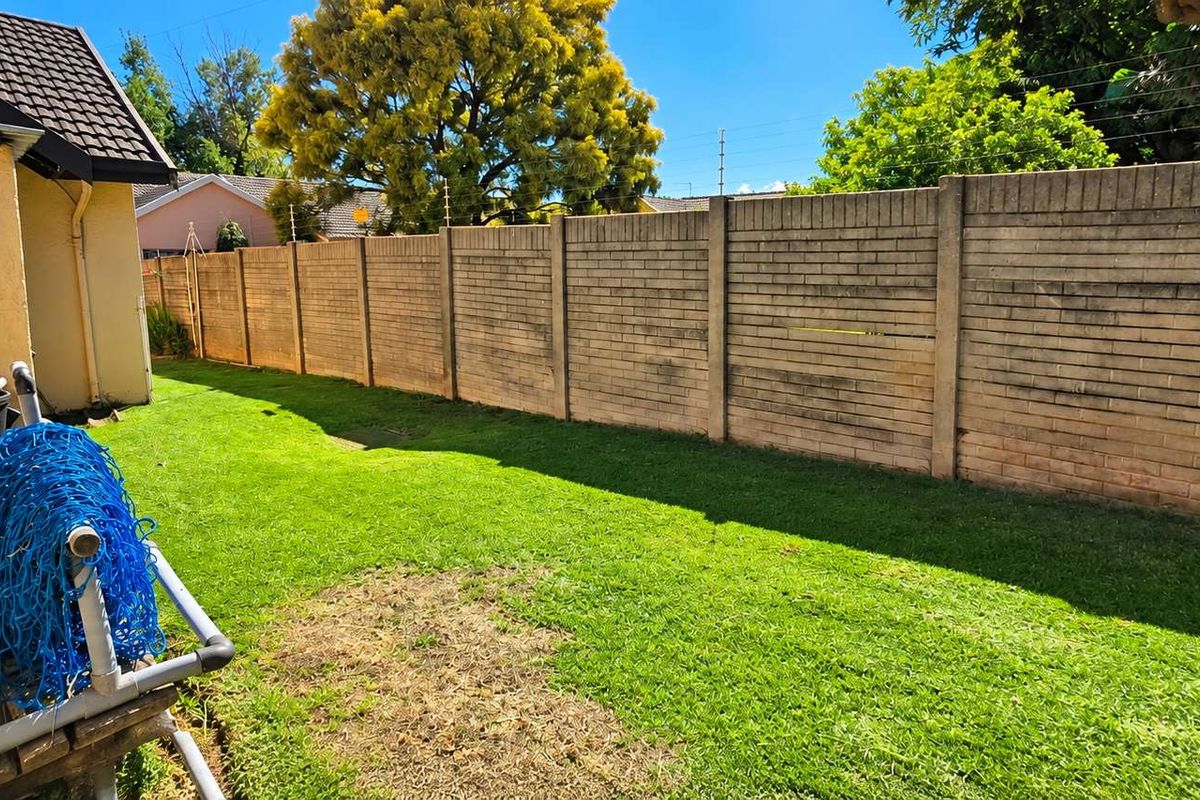 A private rear garden area featuring a lawn and a high precast concrete boundary wall equipped with electric fencing for added security.