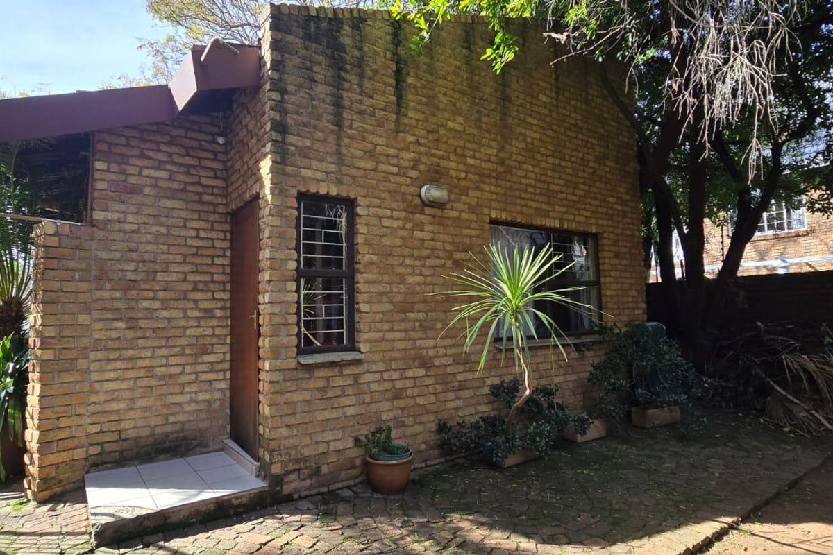 A view of the rear exterior brick facade featuring a single door, window with security bars, and paved patio area.