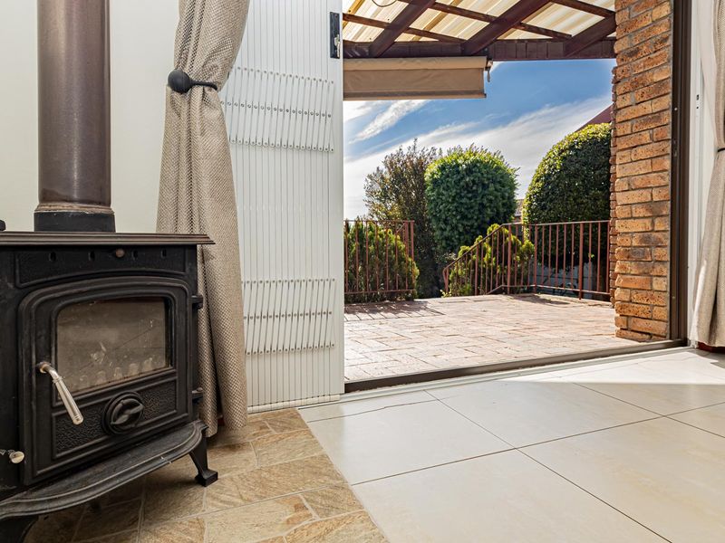 A bright living area featuring a cast iron fireplace and tiled flooring, with seamless access to a covered outdoor patio through sliding glass doors.