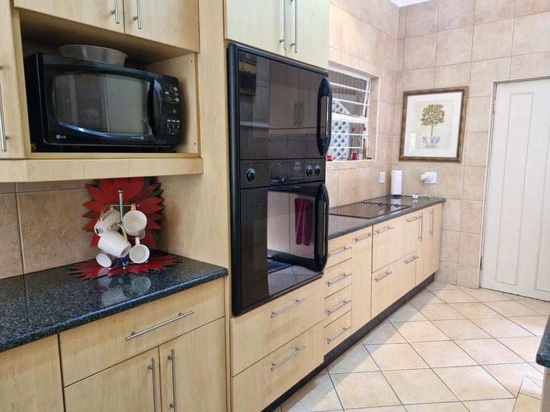 A functional kitchen featuring light wood cabinetry, granite countertops, tiled walls, and integrated appliances including a built-in oven and microwave.