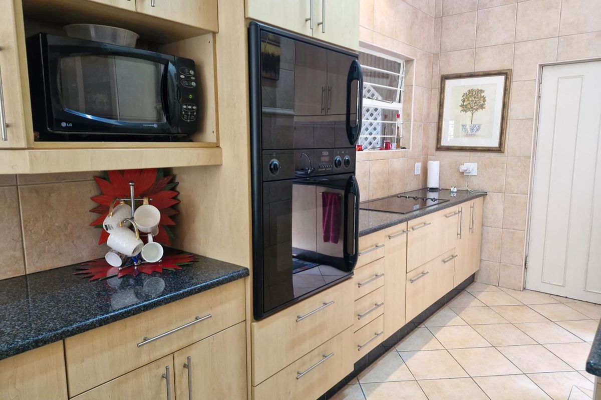 A functional kitchen featuring light wood cabinetry, granite countertops, tiled walls, and integrated appliances including a built-in oven and microwave.
