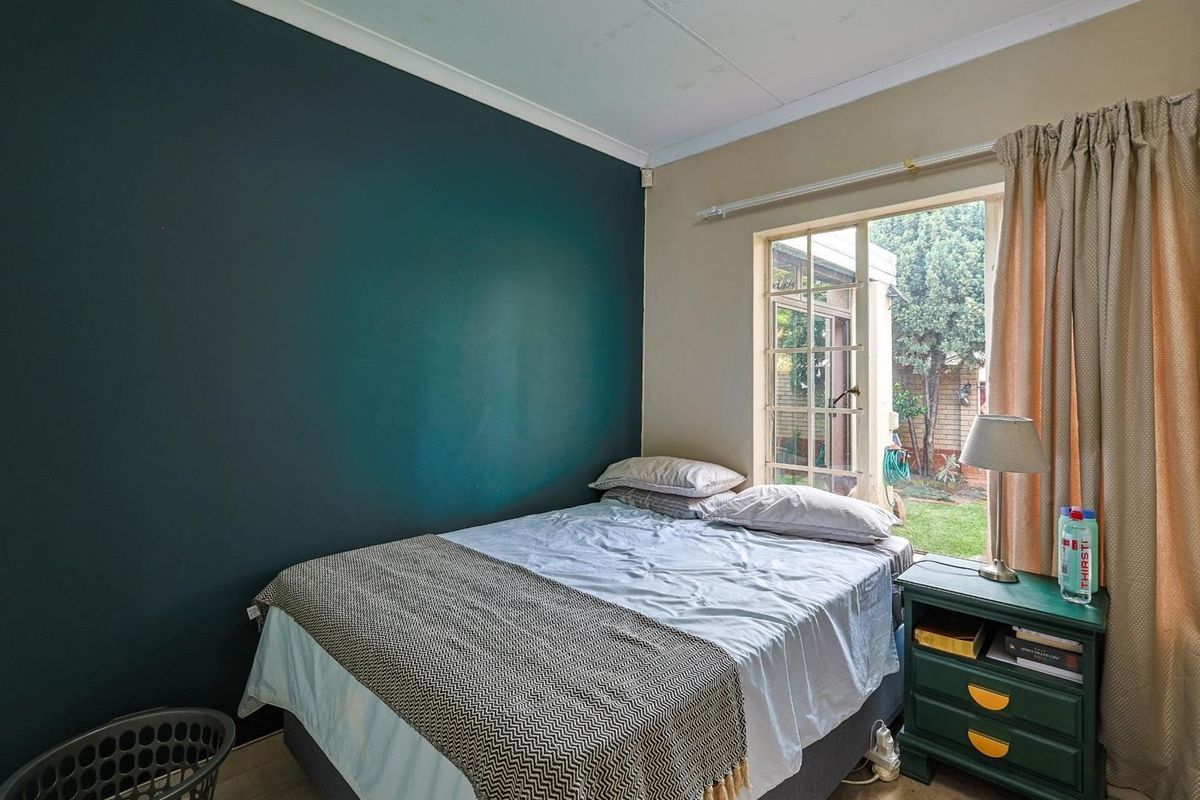 A bedroom featuring a dark accent wall, tiled flooring, and a large window providing natural light and views of the rear garden.