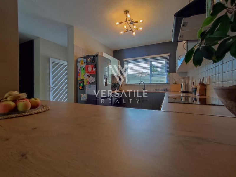 A functional kitchen featuring built-in cabinetry, a tiled backsplash, a hob with an extractor fan, and a central island, illuminated by a modern light fixture.