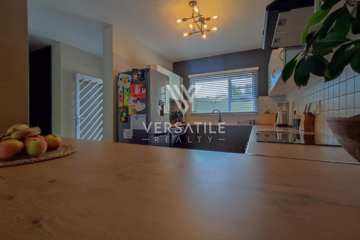 A functional kitchen featuring built-in cabinetry, a tiled backsplash, a hob with an extractor fan, and a central island, illuminated by a modern light fixture.