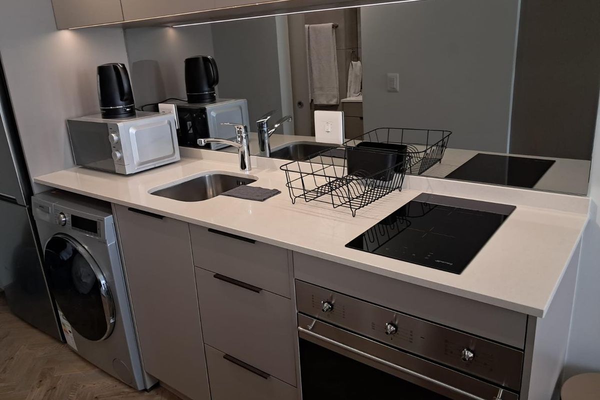 Modern compact kitchen featuring stone countertops, integrated washing machine, built-in oven, induction hob, and a sleek mirrored splashback with under-cabinet lighting.