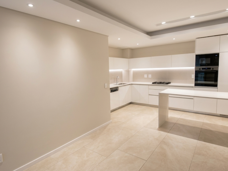 Modern kitchen featuring sleek white cabinetry, integrated appliances, a gas hob, built-in oven, and a functional island, finished with neutral stone tile flooring.