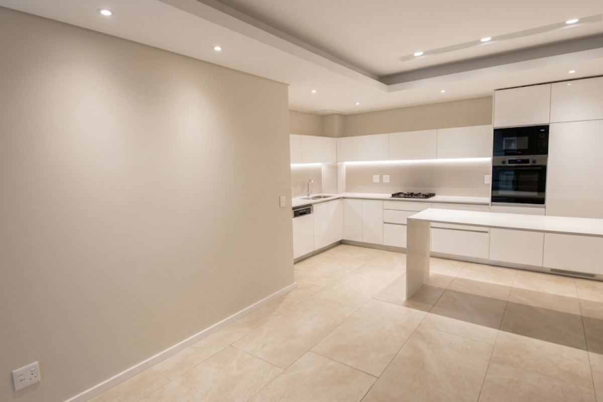 Modern kitchen featuring sleek white cabinetry, integrated appliances, a gas hob, built-in oven, and a functional island, finished with neutral stone tile flooring.