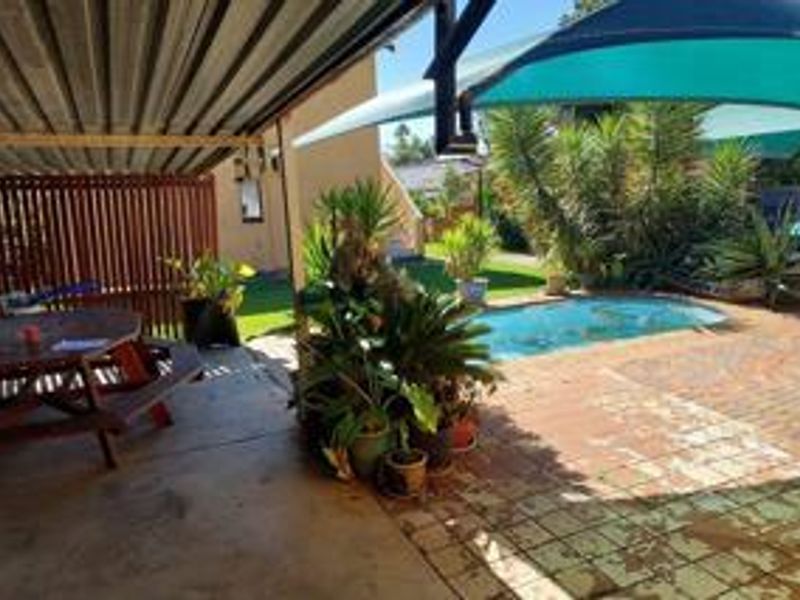 Outdoor entertainment area featuring a covered patio, brick-paved pool deck, and a swimming pool with a shade sail.