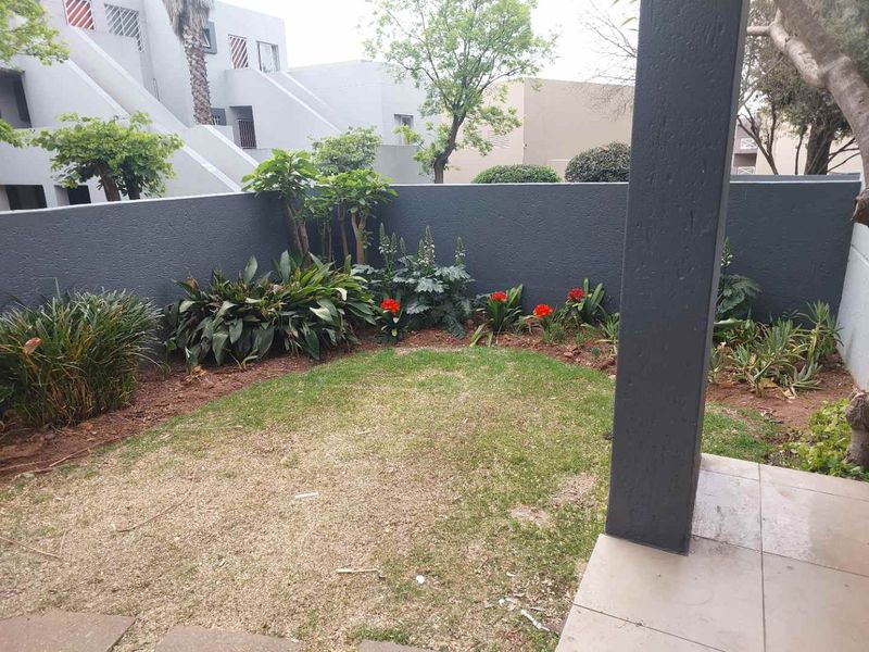 A private rear garden area featuring a small lawn, landscaped garden beds, and a covered tiled patio space.