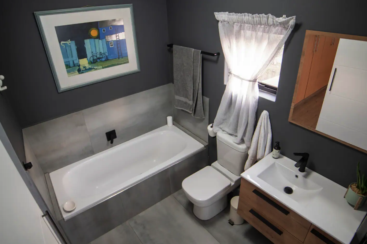 Modern bathroom featuring a built-in bathtub with dark fixtures, a contemporary vanity with integrated sink, and stylish grey tiled finishes.