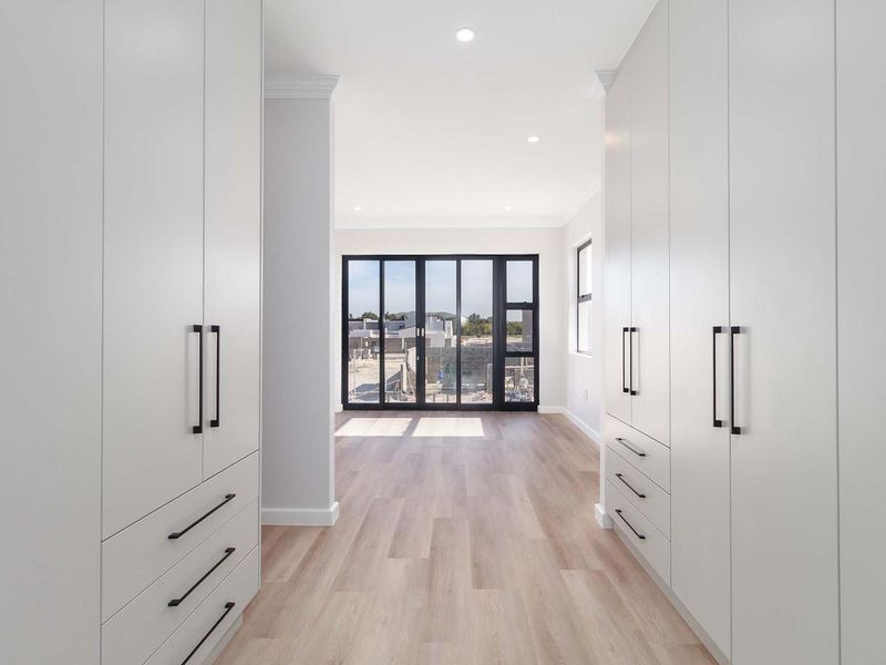 A modern, empty bedroom featuring extensive built-in cabinetry, light wood-look flooring, and large black-framed glass doors leading to an outdoor area.