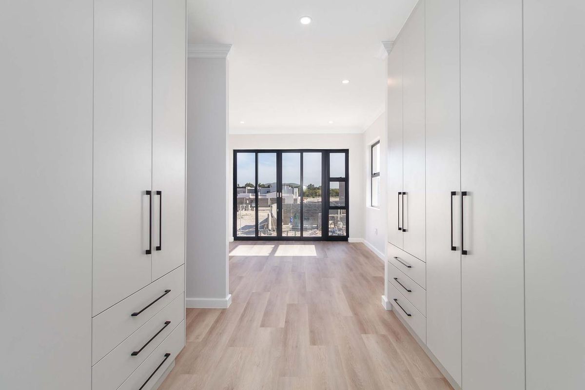 A modern, empty bedroom featuring extensive built-in cabinetry, light wood-look flooring, and large black-framed glass doors leading to an outdoor area.