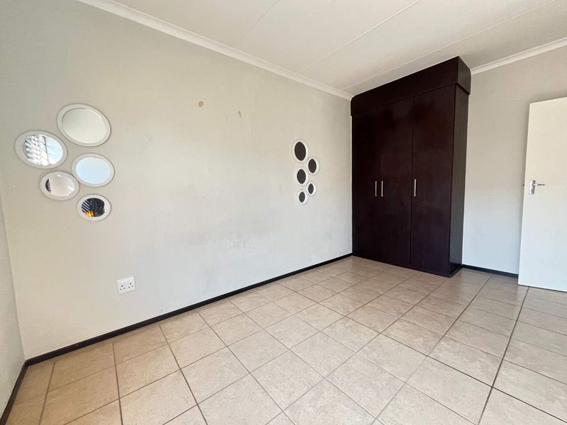 An empty bedroom featuring tiled flooring and a dark wood built-in wardrobe, requiring minor cosmetic wall repairs.