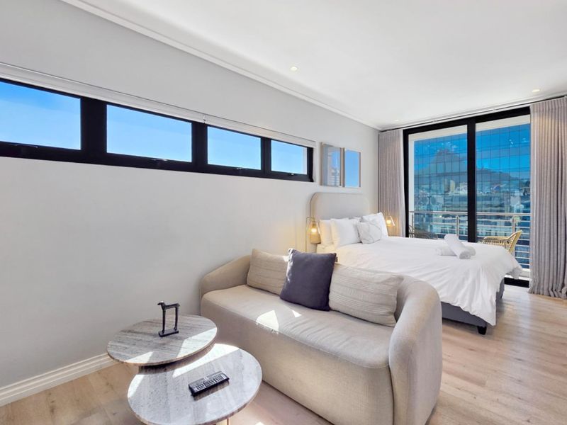 Modern bedroom featuring light laminate flooring, clerestory windows, and large sliding glass doors leading to a balcony with city views.
