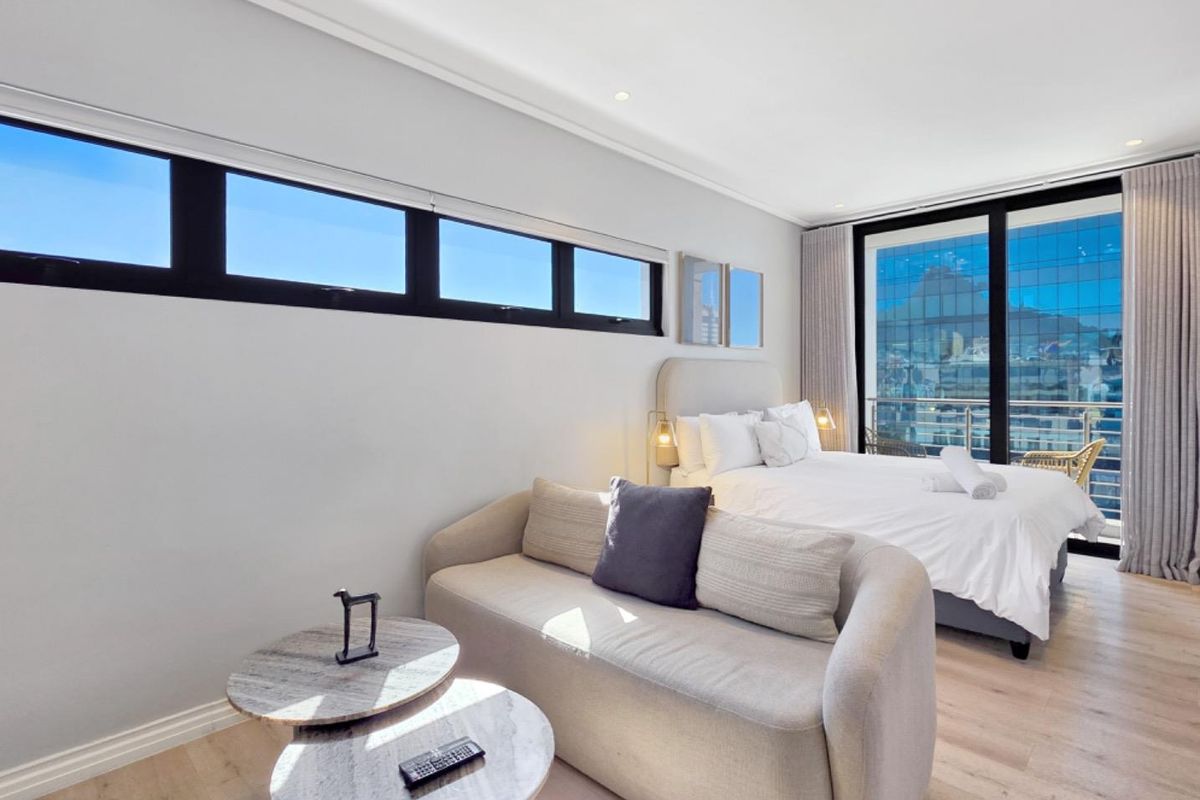 Modern bedroom featuring light laminate flooring, clerestory windows, and large sliding glass doors leading to a balcony with city views.