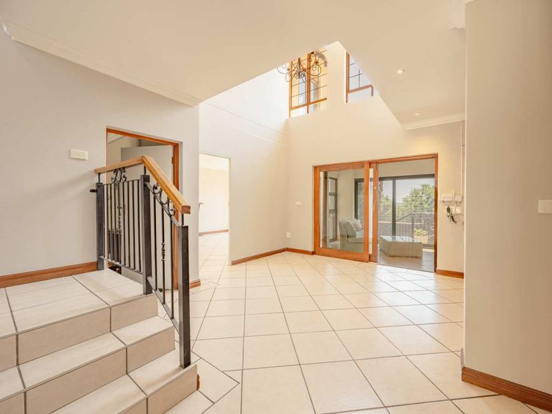 Spacious double-volume entrance hall featuring tiled flooring, a feature staircase with metal balustrade, and large sliding doors leading to an outdoor patio area.