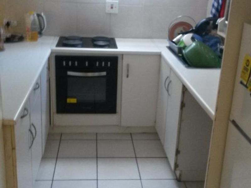 Compact kitchen featuring white cabinetry, tiled flooring, built-in oven, and electric hob, requiring minor repairs to cabinetry.
