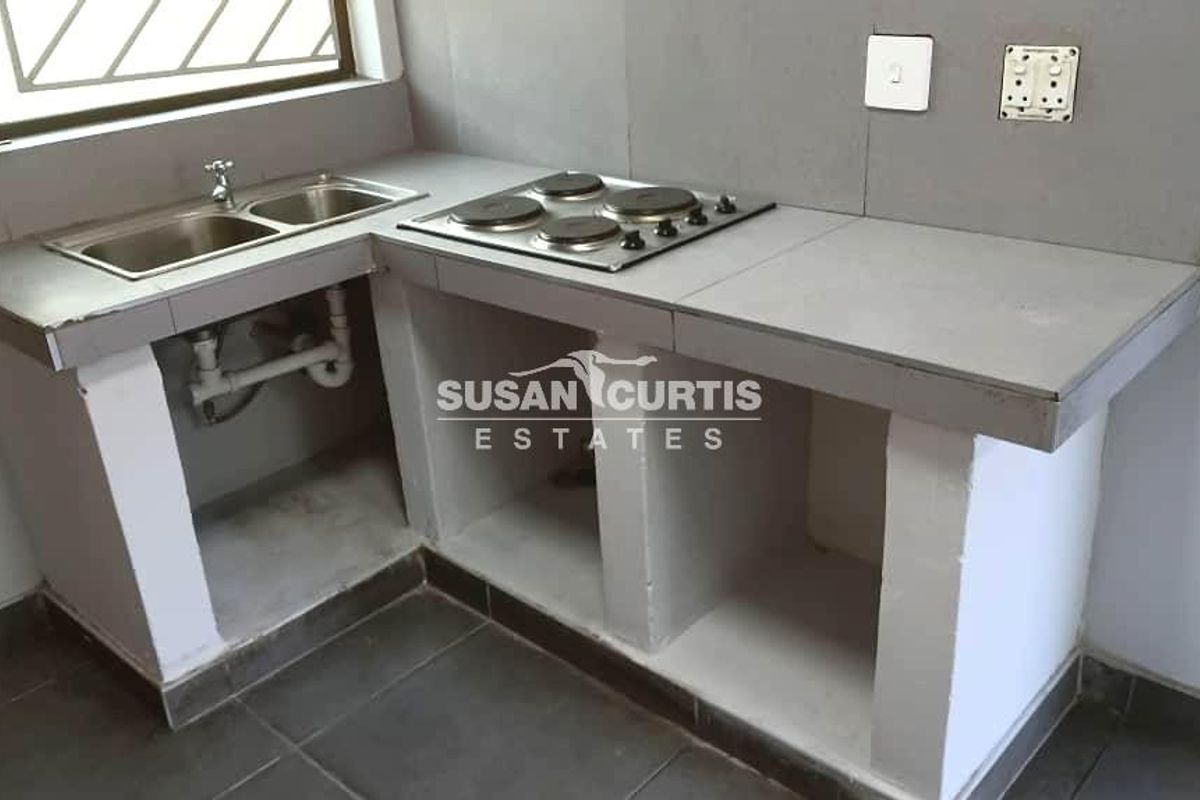 A compact kitchen area featuring a built-in concrete countertop, stainless steel sink, and integrated electric hob with open storage shelving below.