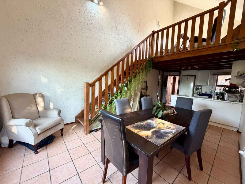 Open-plan living and dining area featuring a wooden staircase leading to a mezzanine level, tiled flooring, and an integrated kitchen space.