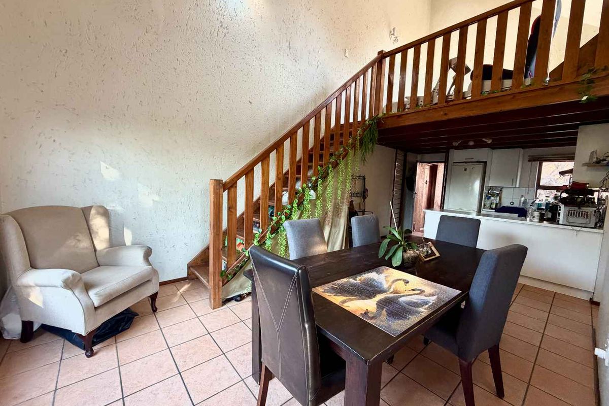 Open-plan living and dining area featuring a wooden staircase leading to a mezzanine level, tiled flooring, and an integrated kitchen space.