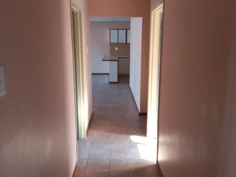 A simple residential hallway with tiled flooring leading towards an open plan kitchen area.