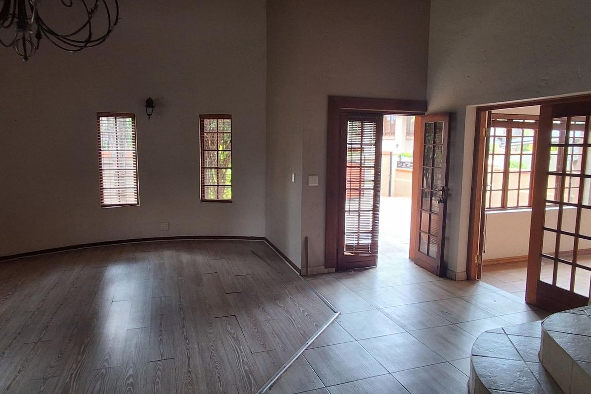 Spacious living area featuring laminate flooring, large windows, and double doors leading to an outdoor space, with a staircase visible to the side.
