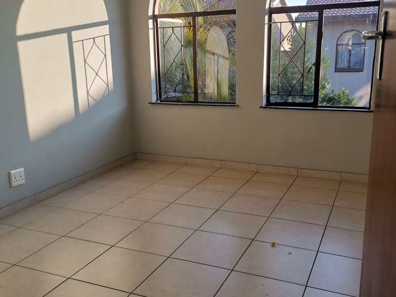 An empty bedroom featuring arched windows with security bars and neutral tiled flooring, offering a bright and versatile space.
