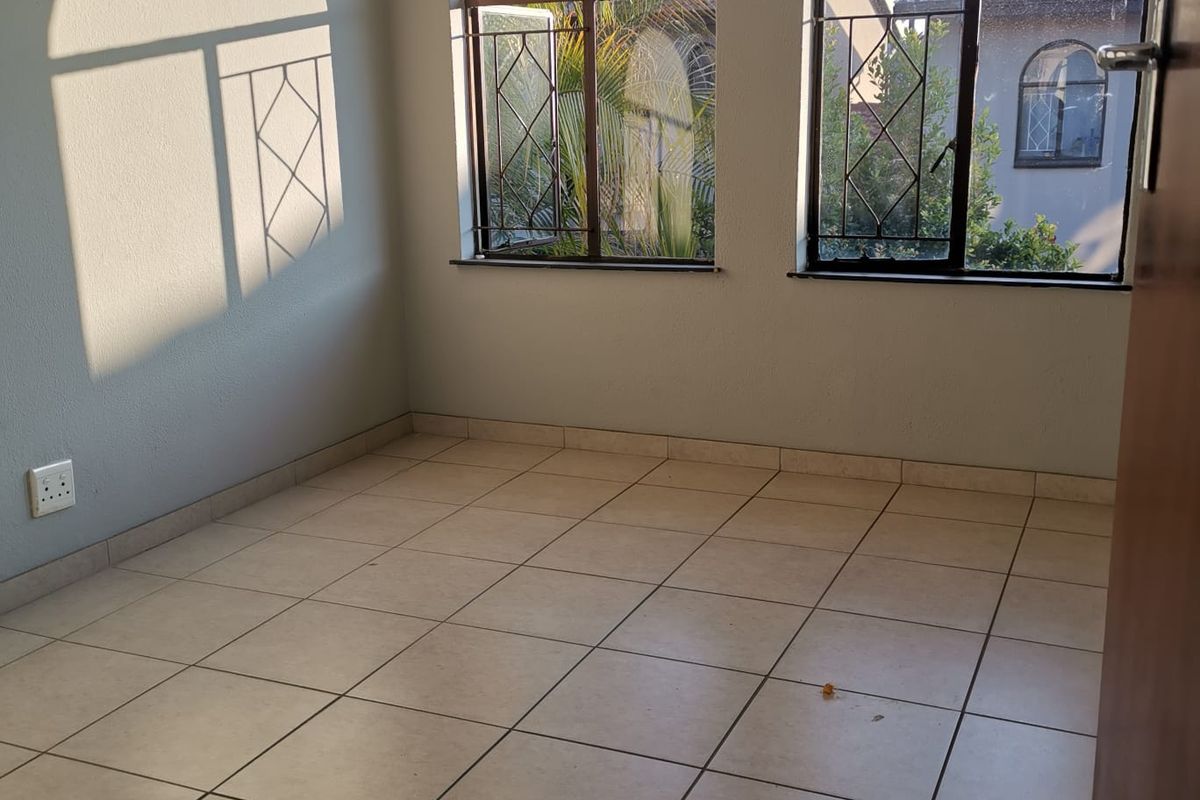 An empty bedroom featuring arched windows with security bars and neutral tiled flooring, offering a bright and versatile space.