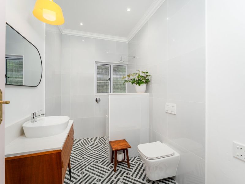 Modern bathroom featuring a wall-mounted toilet, vanity with vessel sink, patterned floor tiles, and a walk-in shower area with white wall tiling.
