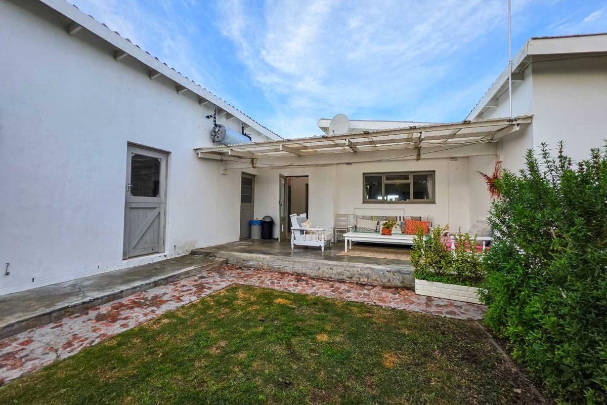 Rear exterior view featuring a covered patio area, lawn, and stone pathway, showing signs of wear and requiring maintenance.